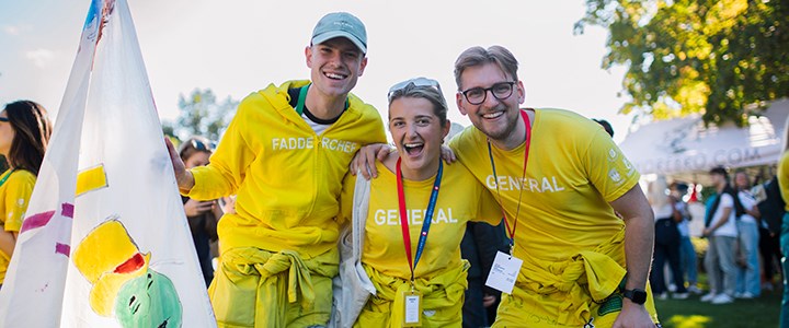 Tre studenter i overaller är glada och tittar in i kameran.