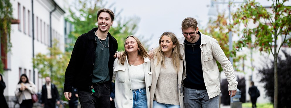 Fyra studenter går och skrattar tillsammans på campus