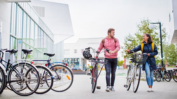 Två studenter leder sina cyklar på campus.