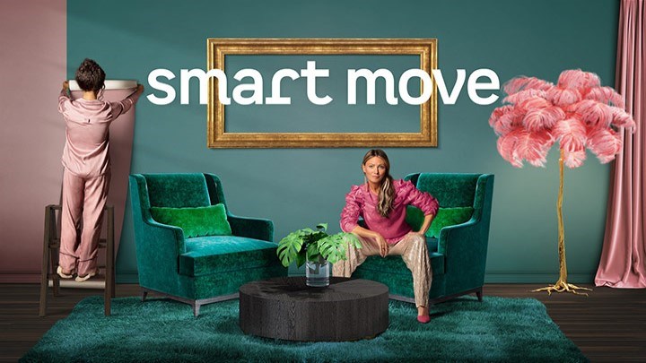 En kvinna sitter i en fåtölj och en annan kvinna hänger upp tyg på väggen. På väggen står det "smart move"