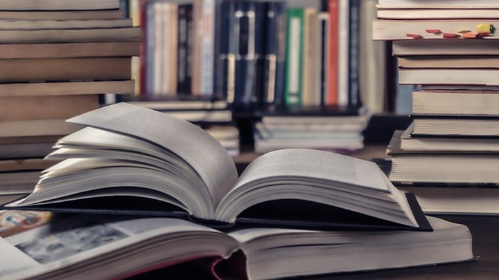 Photo of two open books surrounded by tall stacks of books.