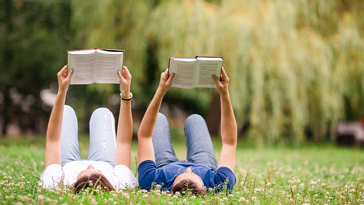 Två personer ligger i gräset och läser varsin bok.