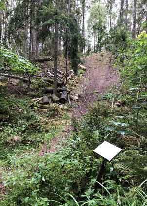 En stig i skogen uppför en brant backe. En skylt nedanför backen.