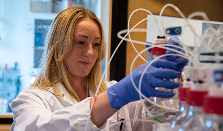 Maria Björnsdotter i vit labbrock flyttar på en genomskinlig flaska med vatten.