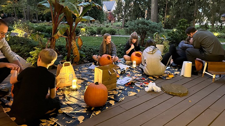 Barn och vuxna sitter på en filt och skär pumpor till halloween.