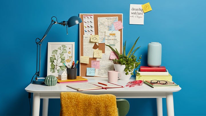 Foto på ett skrivbord med en anslagstavla, böcker och anteckningsblock.