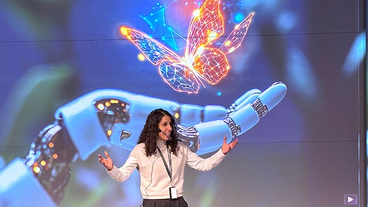 A person speaking in front of a large screen picturing a robot hand and a butterfly.