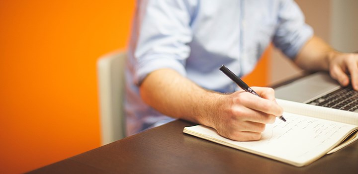 Photo of a man who sits by a table with a pen and a paper.