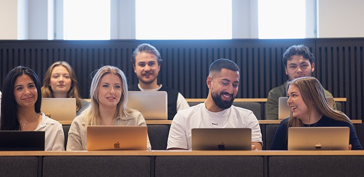 Studenter sitter med sina datorer i en föreläsningssal.