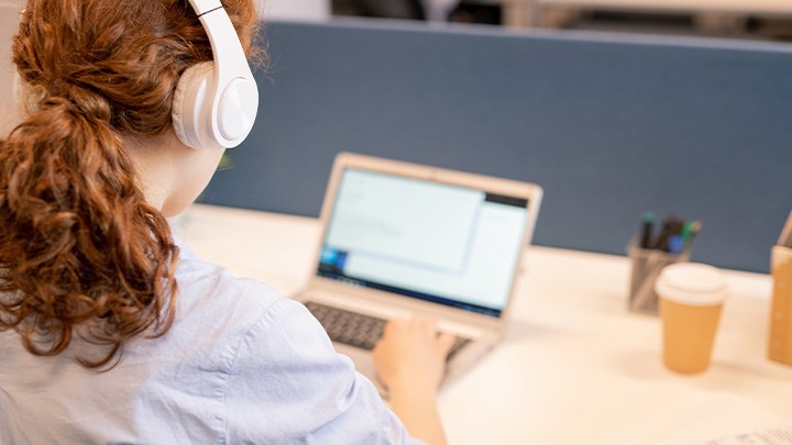 Foto på en person som sitter med hörlurar vid en dator.