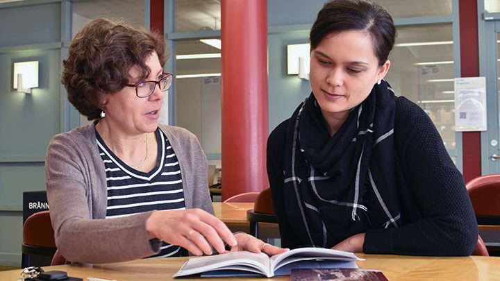 Photo of  two people sitting at a table with a book.