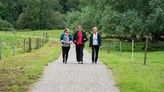 Three people walking on a gravel path in a scenic area.