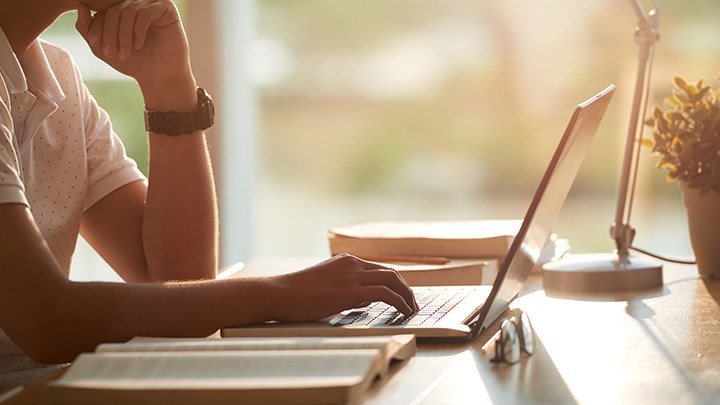 A man is sitting with a computer in front of him and a book beside him.