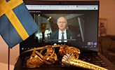 Rektor Johan Schnürer på en datorskärm med svenska flaggan och serpentiner framför. 