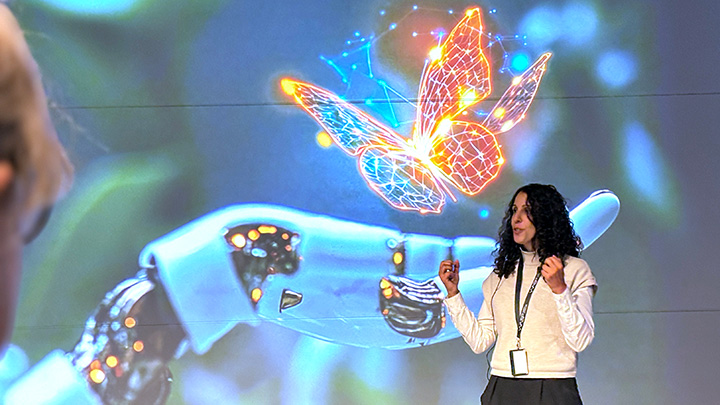 A person speaking in front of a large screen picturing a robot hand and a butterfly.