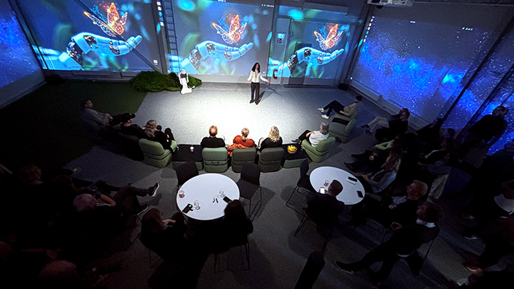 A person speaking to a large audience in front of a large screen picturing a robot hand and a butterfly.