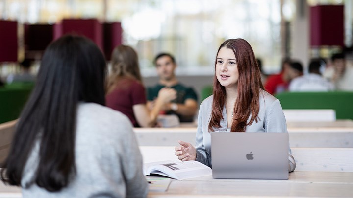 Foto på två studenter som sitter vid ett bord med datorer.