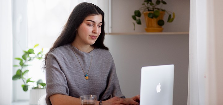 En kvinnlig student sitter vid ett köksbord och skriver på en laptop.
