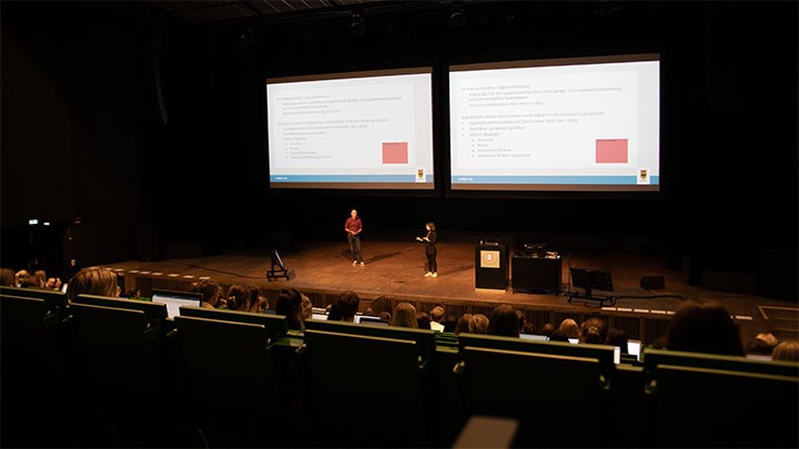 Aula Nova - föreläsare på scenen och studenter i publiken.