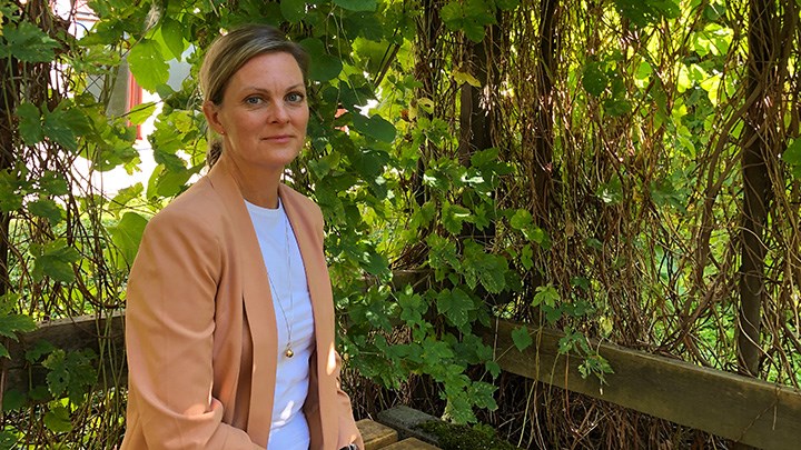 Anna-Karin Larsson sitter i en pergola med gröna blomrankor. 