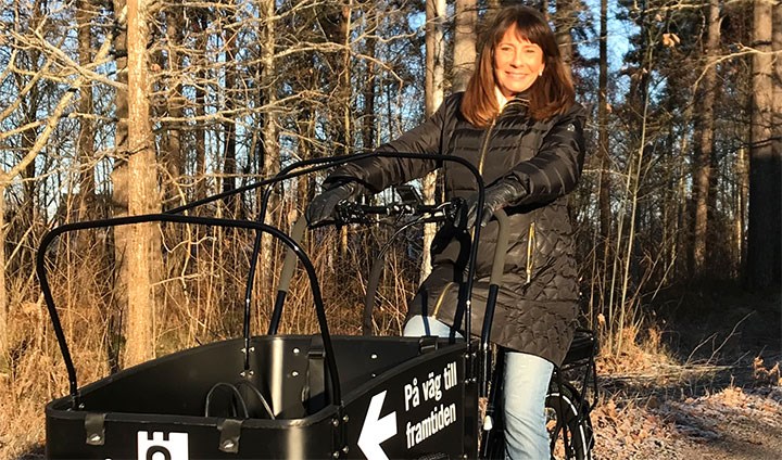 Barbro Bergfeldt i solig utomhusmiljö på en svart lådcykel med Örebro universitets logotyp på.