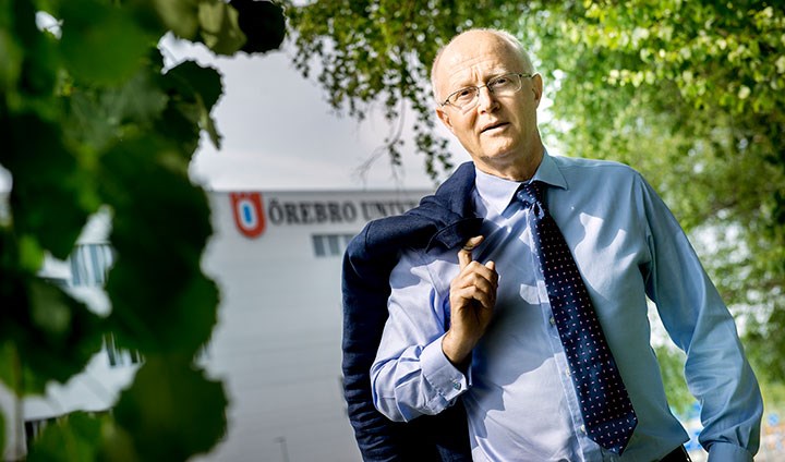 Johan Schnürer står framför Örebro universitet. Han har kavajen slängd över ena axeln.