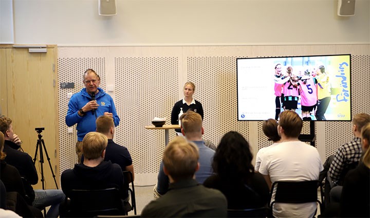 Två personer föreläser inför en publik av studenter.