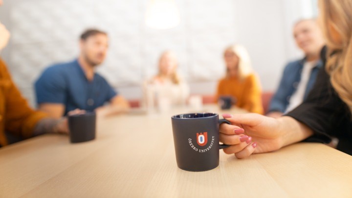människor runt ett bord med en kaffekopp i fokus