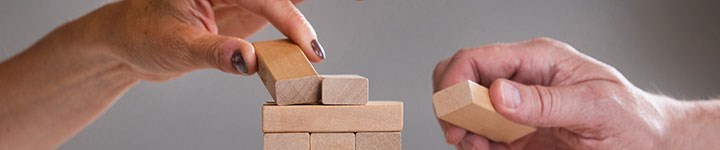 A female and a male hand build a tower of bricks. There is a British flag in the right corner.