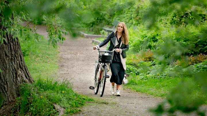 Kvinna leder cykel genom gr&ouml;nska 