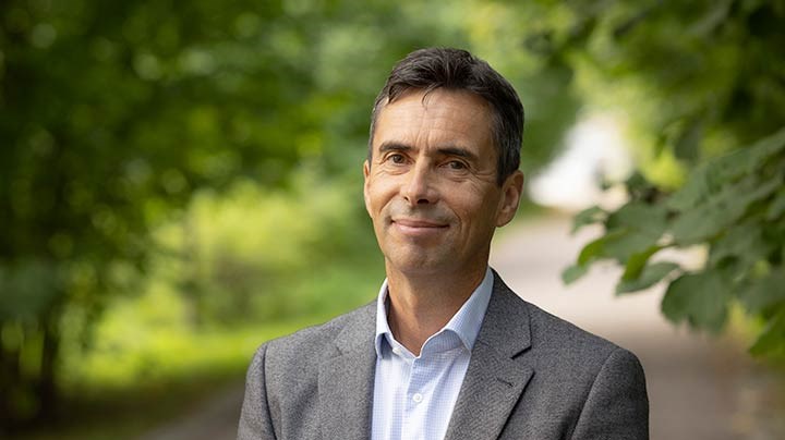 Andreas Bergh standing in front of a country lane bordered by trees.