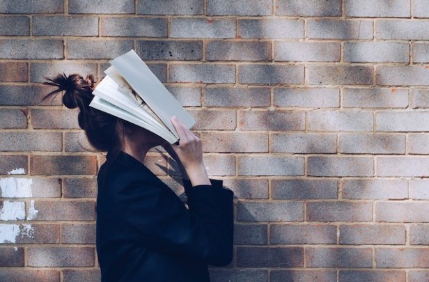 Person står upp och håller upp en bok framför ansiktet