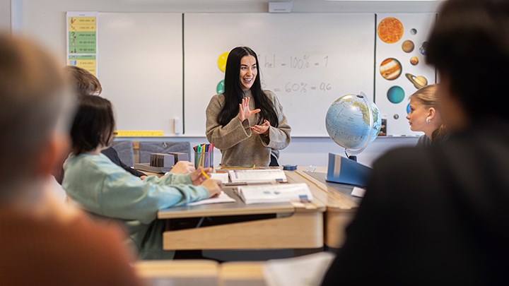 En kvinnlig lärare framför en skolklass i ett klassrum.